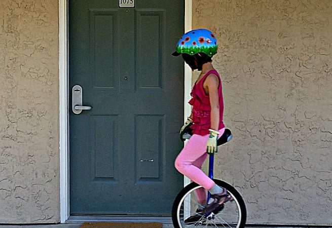Girl on unicyle rolls by motel door